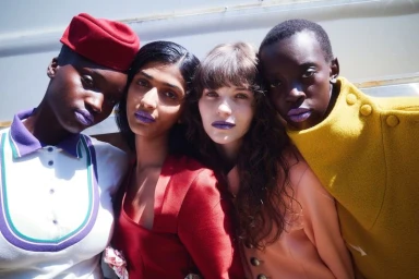 Four female models with purple lipstick posing together outdoors for AnOther Magazine editorial.