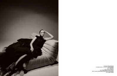 Woman in a black dress reclining on a quilted designer sofa against a neutral studio backdrop for Schon Magazine interview