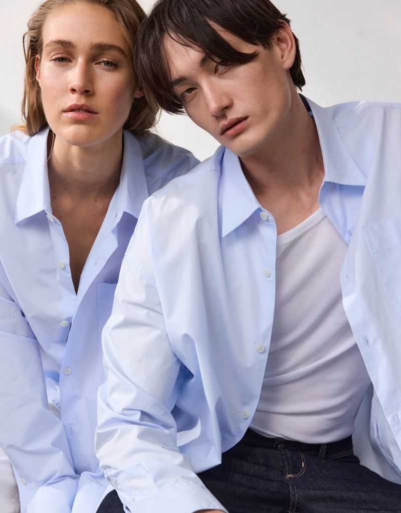 Two models wearing light blue button-down shirts against a plain white studio background photographed by Tina Luther
