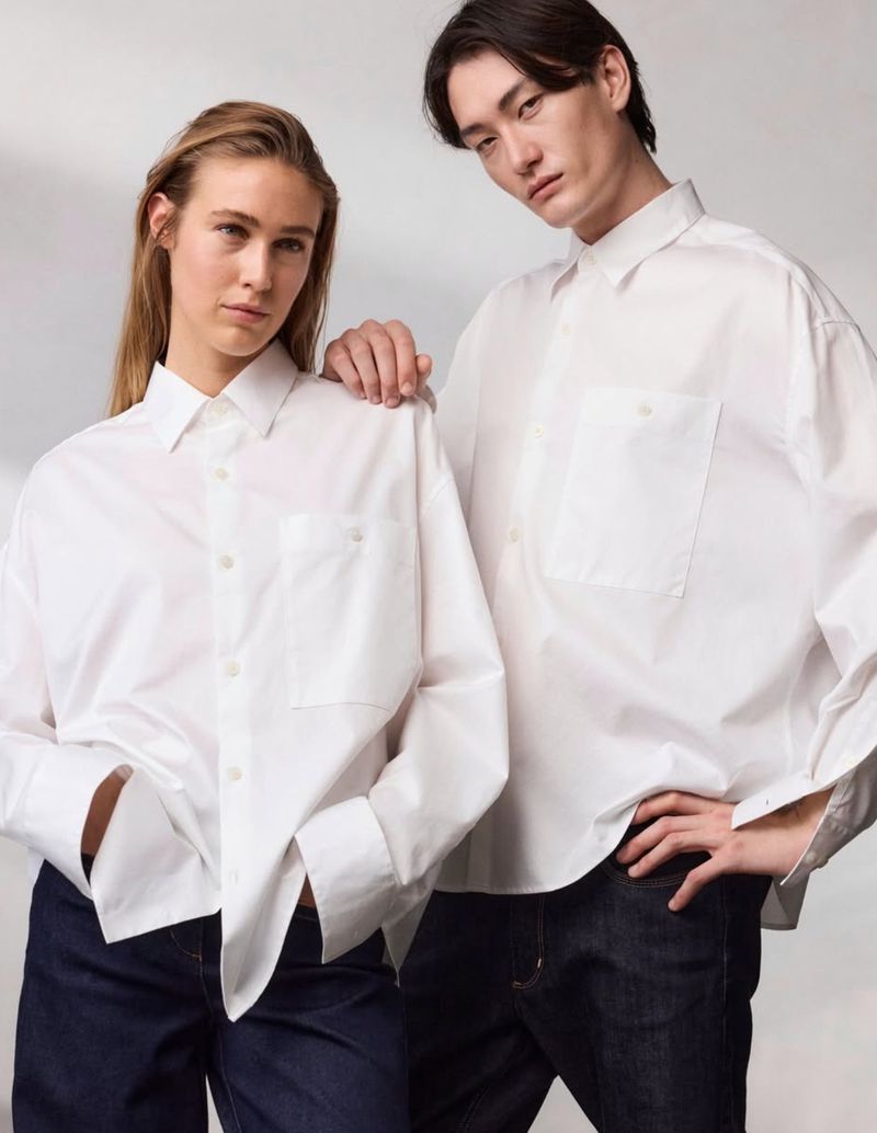 Two models wearing white button-down shirts and dark trousers against a seamless light grey studio background.