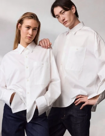 Two models wearing white button-down shirts and dark trousers against a seamless light grey studio background.