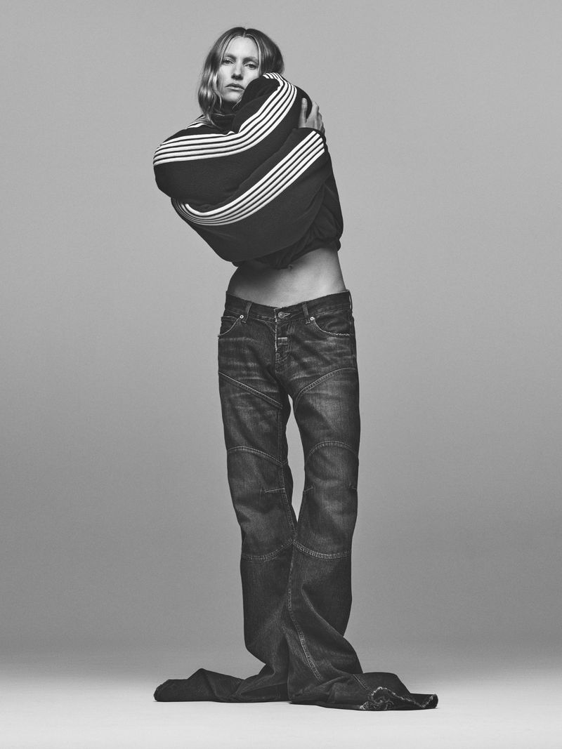 Monochrome studio portrait of a slender adult posing in a striped, long-sleeve sweater and dark, oversized jeans.