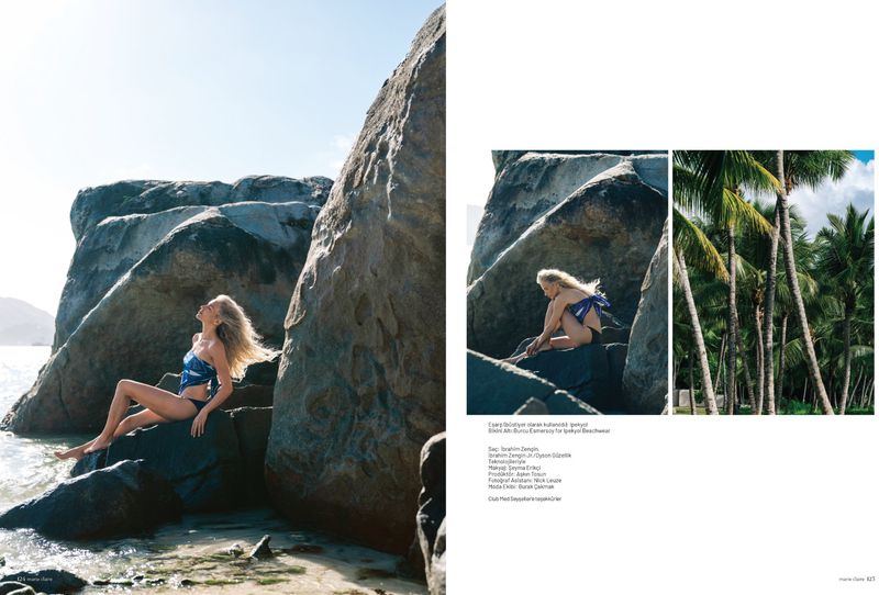 Editorial magazine layout featuring a blonde woman in a blue patterned top and black swimwear posed among large coastal rocks