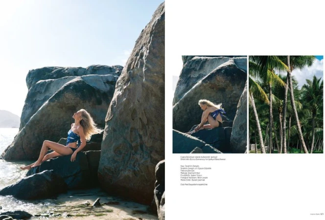 Editorial magazine layout featuring a blonde woman in a blue patterned top and black swimwear posed among large coastal rocks