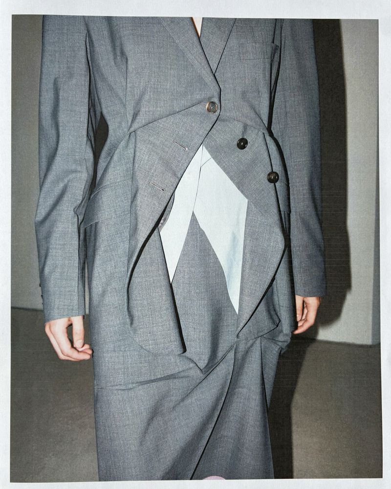 Close-up of a tailored grey blazer and skirt set featuring asymmetrical draping and a pale insert