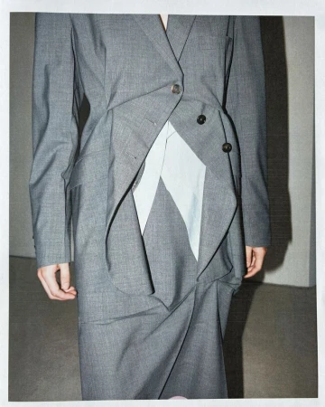 Close-up of a tailored grey blazer and skirt set featuring asymmetrical draping and a pale insert