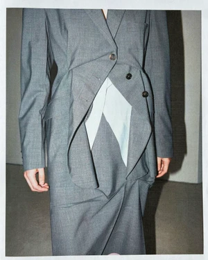 Close-up of a tailored grey blazer and skirt set featuring asymmetrical draping and a pale insert