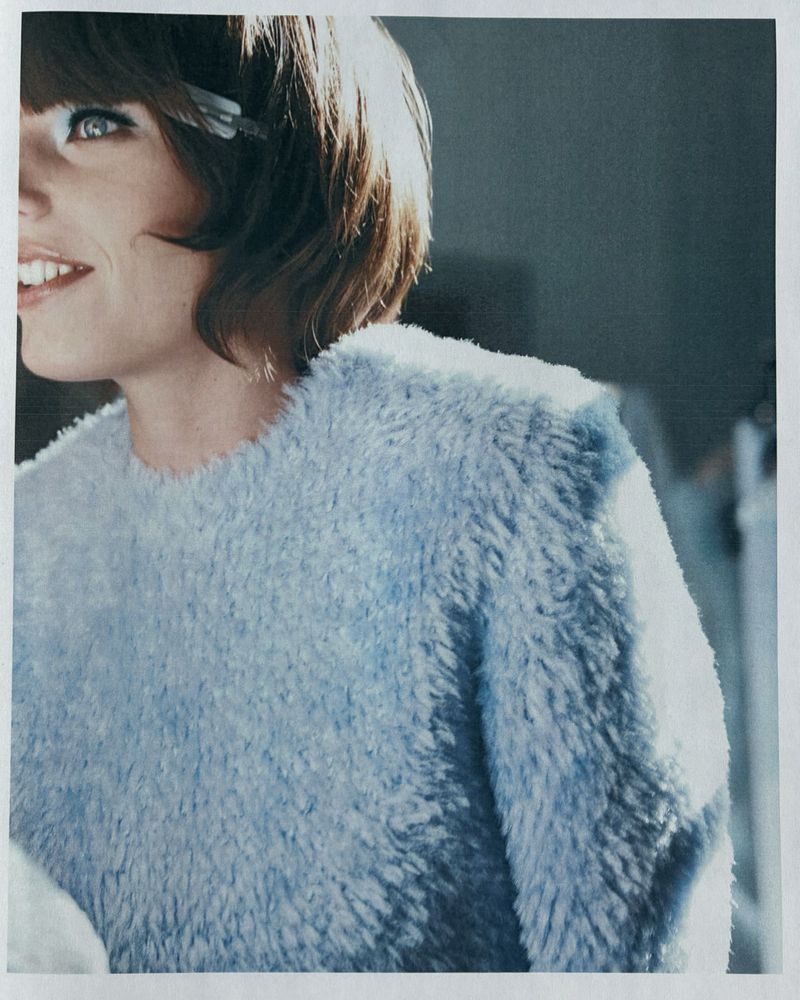 Close-up portrait of a smiling woman wearing a textured powder blue sweater with visible hair clips.