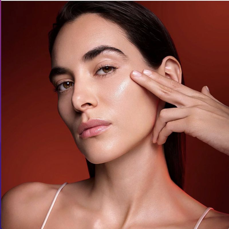 Close-up beauty portrait of a woman touching her cheek against a warm red background for YSL Beauty