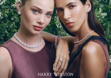 Two female models wearing diamond necklaces and earrings against a lush green garden background for Harry Winston.