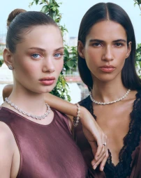 Two female models wearing diamond necklaces and fine jewellery outdoors against a soft natural greenery background.