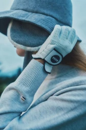 Close-up of a person wearing a light blue bucket hat, ribbed sweater, and golf glove for Hugo GOLF