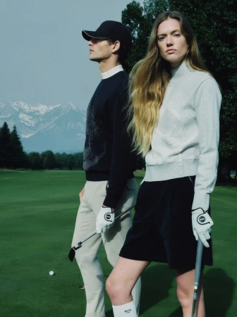 A man and a woman in golf attire stand on a green fairway with mountains in the background for HUGO golf campaign.
