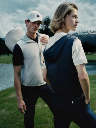 Two models outdoors on a golf course wearing HUGO golf apparel with a lake and mountains in the background.
