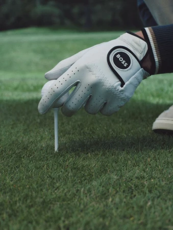 Close-up of a person wearing a white golf glove placing a golf ball on a tee in the grass.