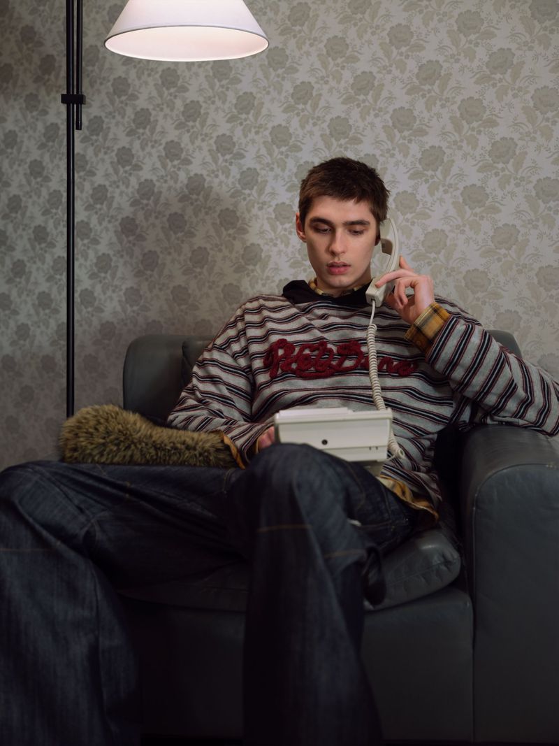 Model seated in an armchair holding a telephone receiver against a patterned wallpaper background for WE11DONE
