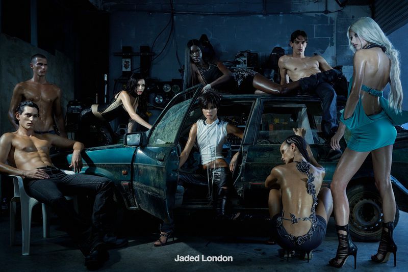 Group of models posing inside and around a vintage teal car in a dimly lit garage for Jaded London AW 26 Campaign.