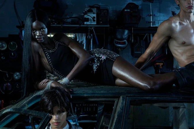Three models posing in a dimly lit garage setting, featuring a woman lying across the roof of a car.