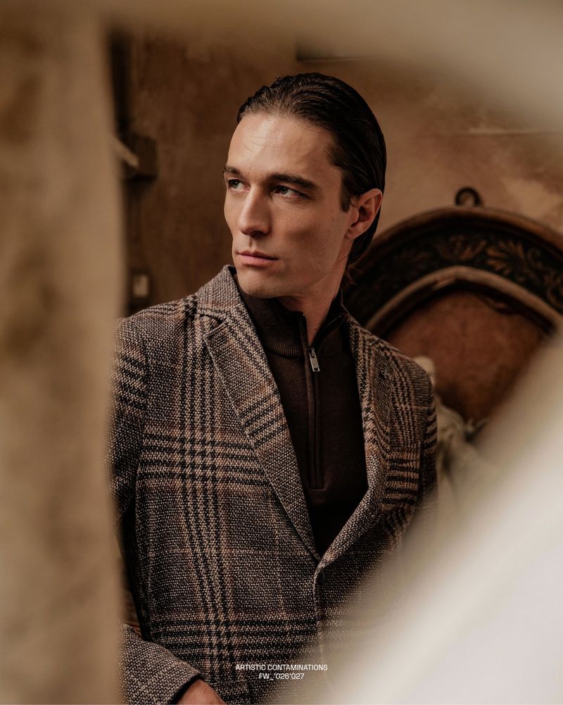 Francesco Mariottini wearing a plaid blazer and dark zip sweater in an indoor editorial portrait for DISTRETTO12.