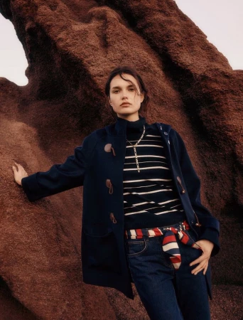 Model wearing a navy duffle coat and striped sweater posing against rugged rock formations for Pennyblack.