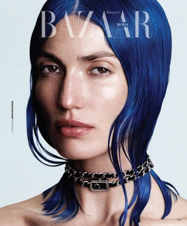 Close up portrait of a woman with vibrant blue hair and a silver chain choker necklace against a light blue background for Harper's Bazaar