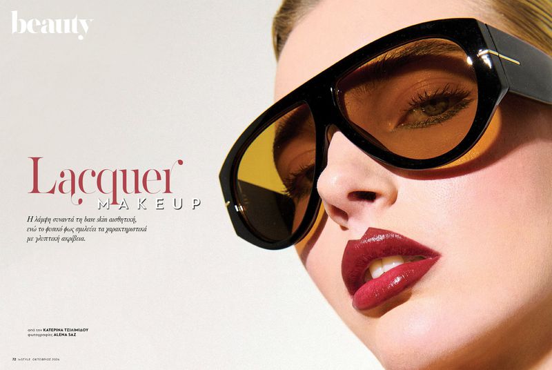 Close-up beauty portrait of a woman wearing oversized black sunglasses and glossy burgundy lipstick against a white background