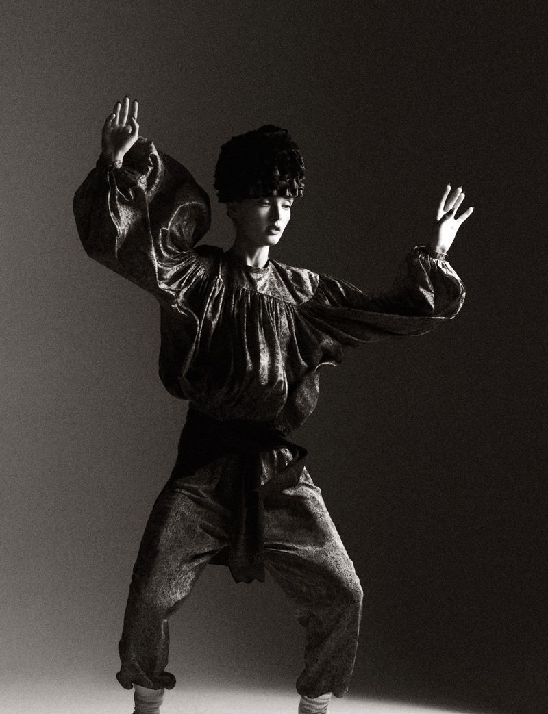 Model in voluminous metallic blouse and trousers posing with arms raised in studio