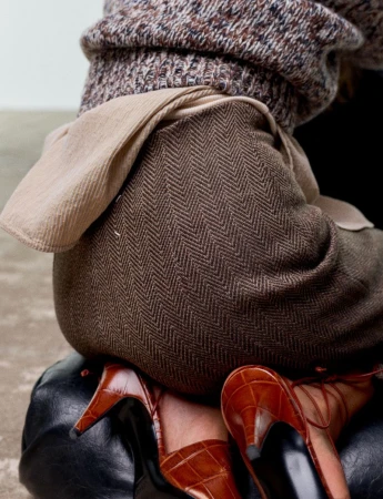 Close-up of a model wearing a herringbone skirt, patterned sweater, and brown leather heels for Harper's Bazaar France
