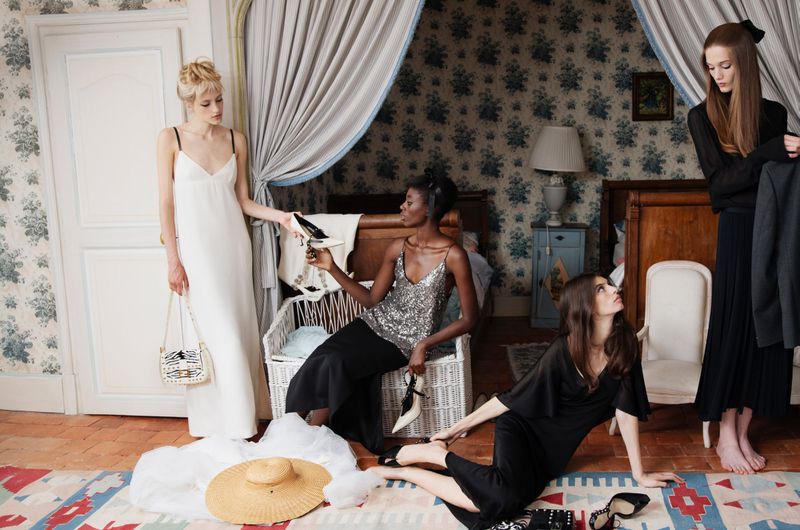 Four female models in a domestic bedroom setting posing with shoes and clothing for an editorial feature.