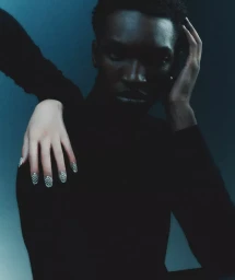 Portrait of a black man in a black turtleneck with a hand resting on his shoulder featuring patterned nail art