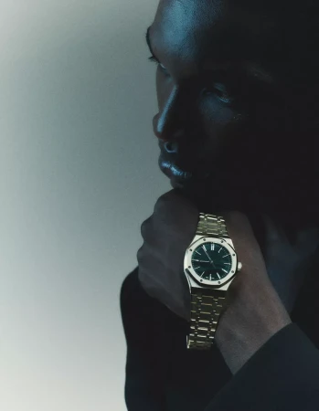 Close-up portrait of a man wearing a metallic gold watch with a dark dial, shot in moody lighting.