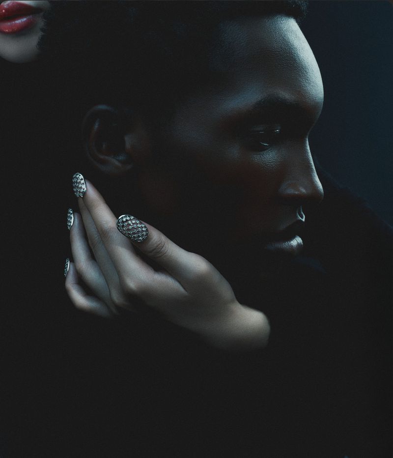 Close-up portrait of a black man with a hand wearing jewelled rings resting gently on his cheek for Sèduction Magazine.