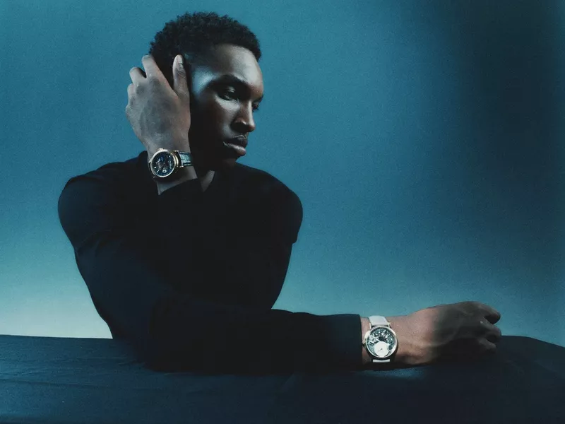 Black man wearing luxury watches posing against a dark blue background for a Sèduction Magazine editorial.