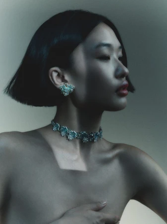 Close-up portrait of a woman wearing ornate floral jewellery including a matching necklace and earrings against a neutral studio background.