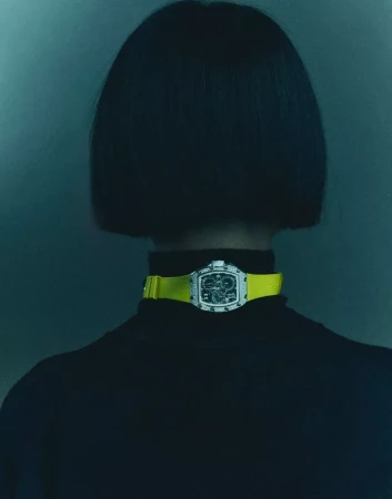 Rear view of a person with short dark hair wearing a black turtleneck and a yellow strapped watch around their neck.