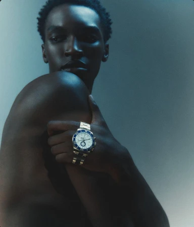 Portrait of a man wearing a luxury wristwatch with a blue bezel and white dial against a moody muted background