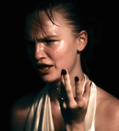 Close-up portrait of a woman with wet hair and glossy skin wearing a white satin halter top against a dark background