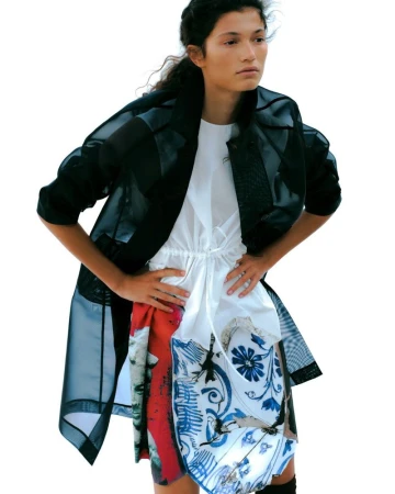 Model Victoria Blecher wearing a sheer black coat over a white patterned dress against white seamless