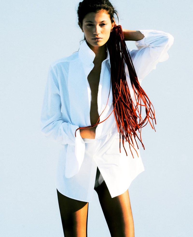 Model in unbuttoned white shirt holding long red cords against bright white background