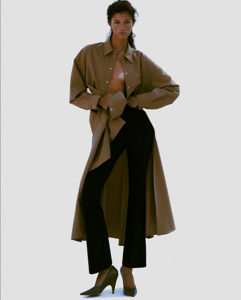 Model wearing a brown open coat and black trousers against a neutral background for a Harper's Bazaar Brazil editorial