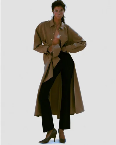 Model wearing a brown open coat and black trousers against a neutral background for a Harper's Bazaar Brazil editorial