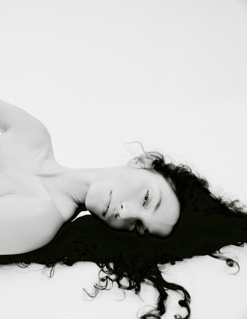 Model lying down with dark hair fanned out against a seamless white background