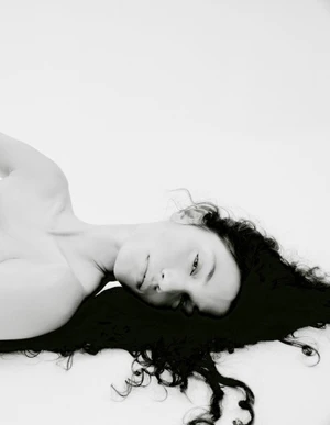 Model lying down with dark hair fanned out against a seamless white background