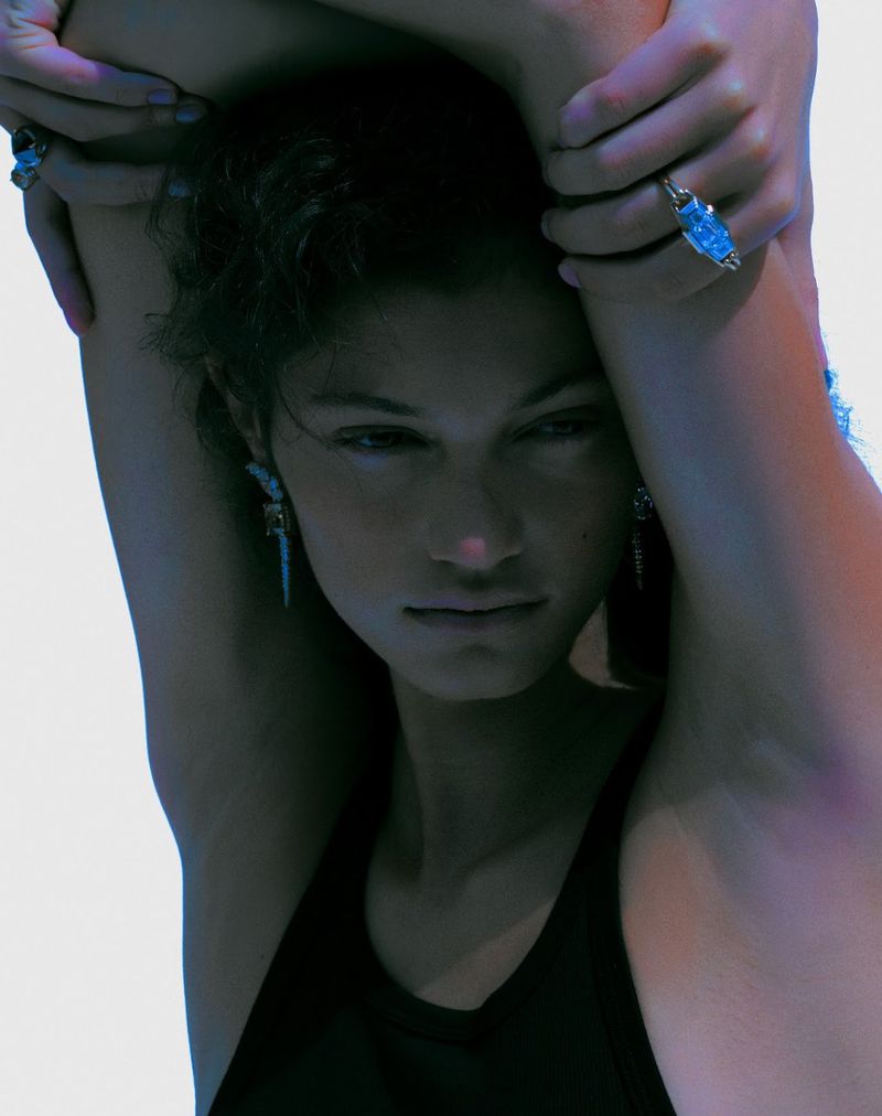 Close-up portrait of model Victoria Blecher with arms raised, wearing statement rings and earrings against a bright seamless white background.