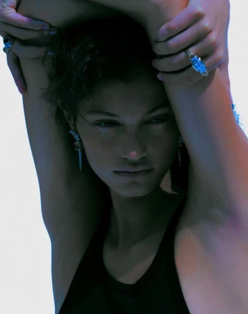 Close-up portrait of model Victoria Blecher with arms raised, wearing statement rings and earrings against a bright seamless white background.