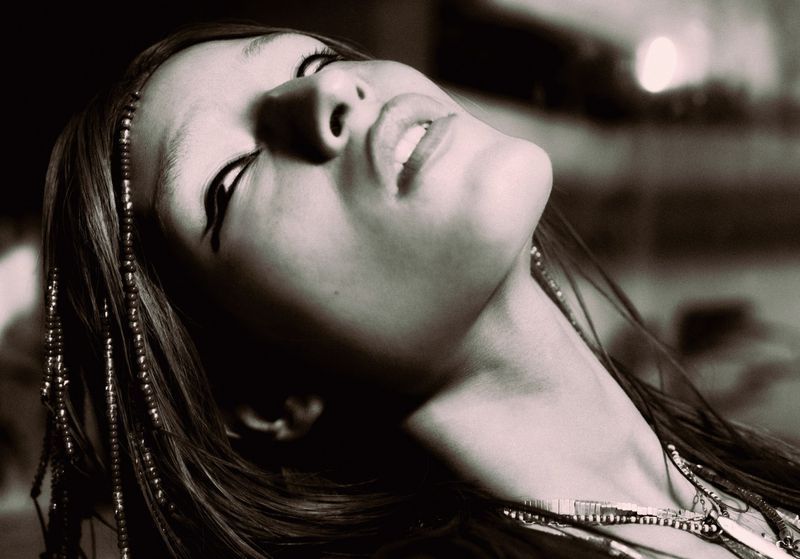 Close-up monochrome portrait of a model with beaded hair tilted back, captured in dramatic low-angle perspective.