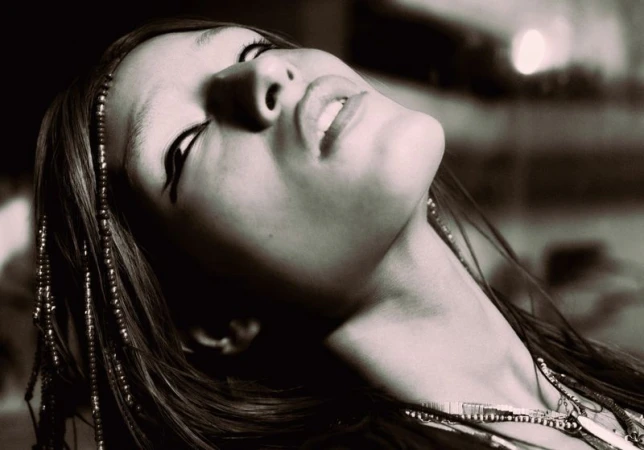 Close-up monochrome portrait of a model with beaded hair tilted back, captured in dramatic low-angle perspective.