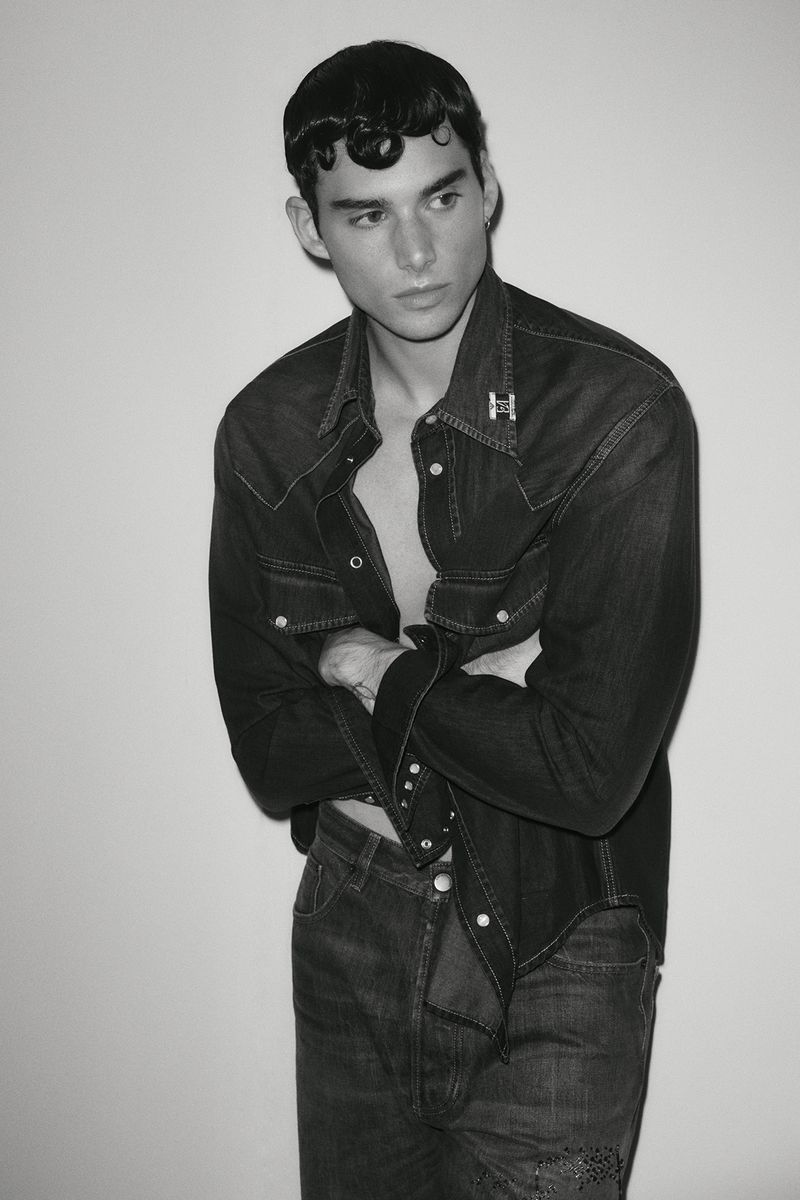 Monochrome portrait of a male model in a dark denim shirt and jeans against a plain background.