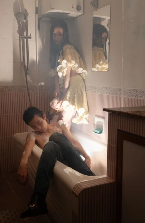 A man seated in a bathtub and a woman standing beside him in a tiled bathroom for an editorial project by Lean Lui.