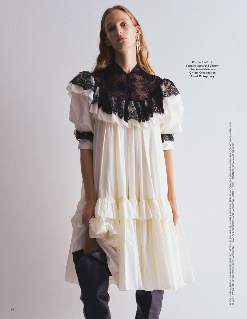 Model Kira Alferink in a ruffled white dress with black lace yoke and dark boots against a grey background